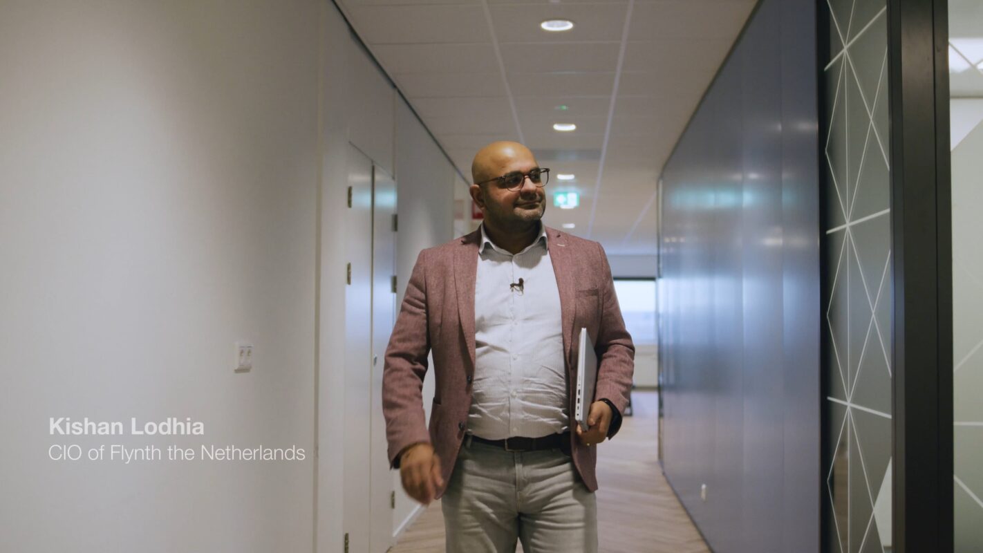 Photo de Kishan Lodhia, CIO de Flynth Netherlands, marchant dans un couloir de bureau avec un ordinateur portable. Flynth a fait don d’équipements informatiques afin de créer un impact sociétal positif et d’améliorer l’accès à la technologie.